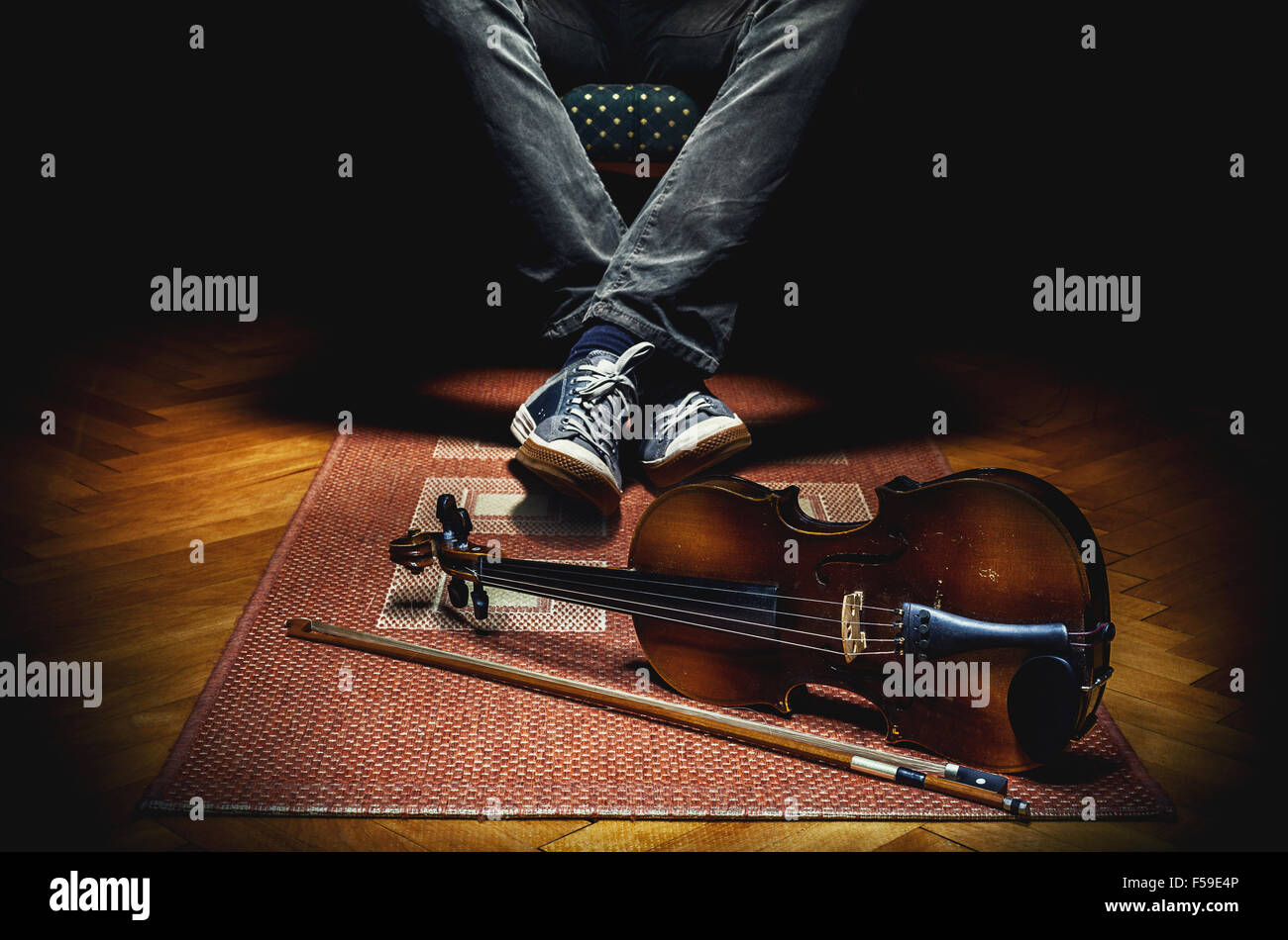 Joueur de violon au repos dans un fauteuil et son violon sur tapis de sol carrelé. Banque D'Images