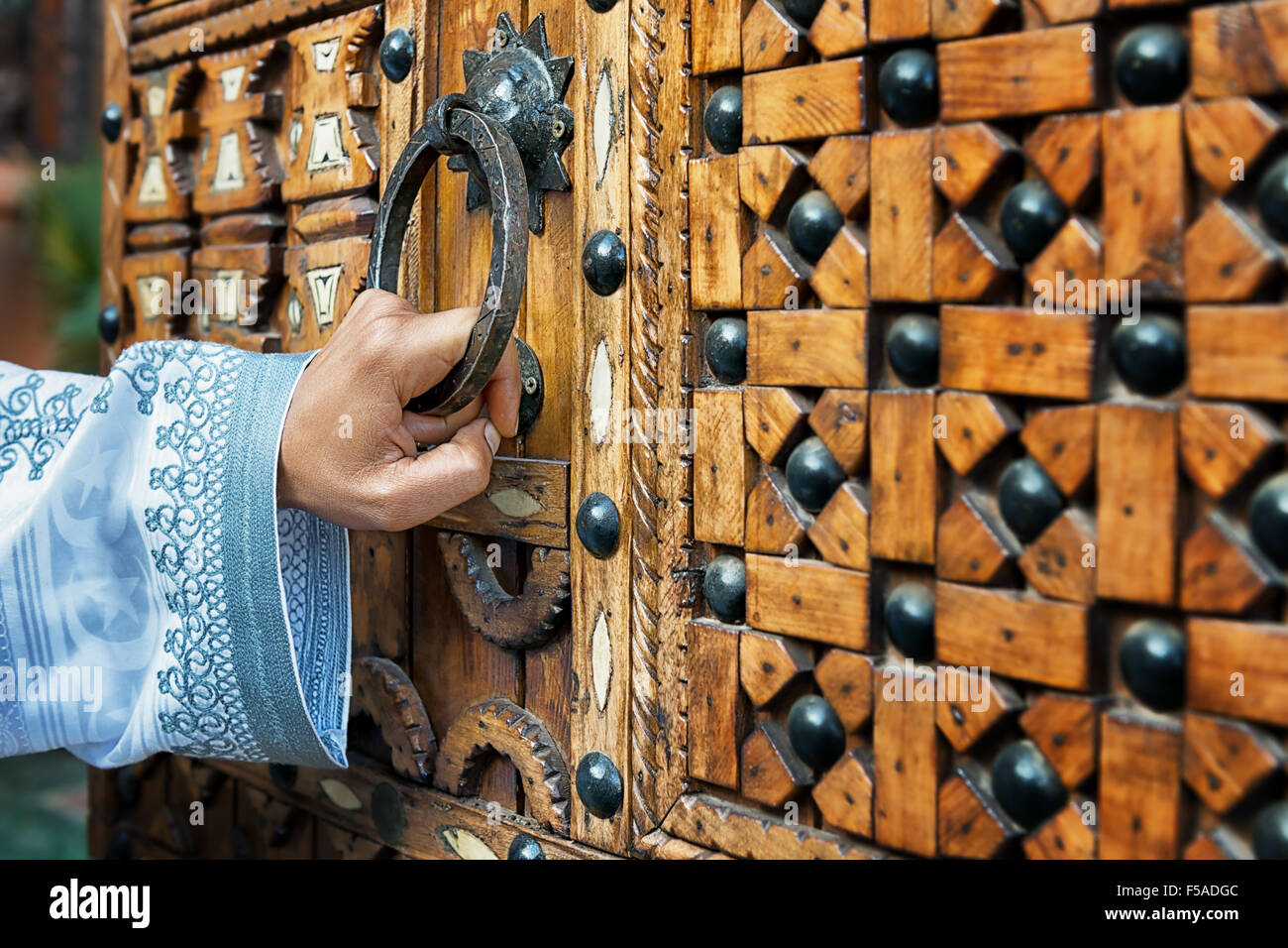 Une main tenant une poignée de porte en bois, d'une traditionnelle marocaine, porte, dans le sud du Maroc. Banque D'Images