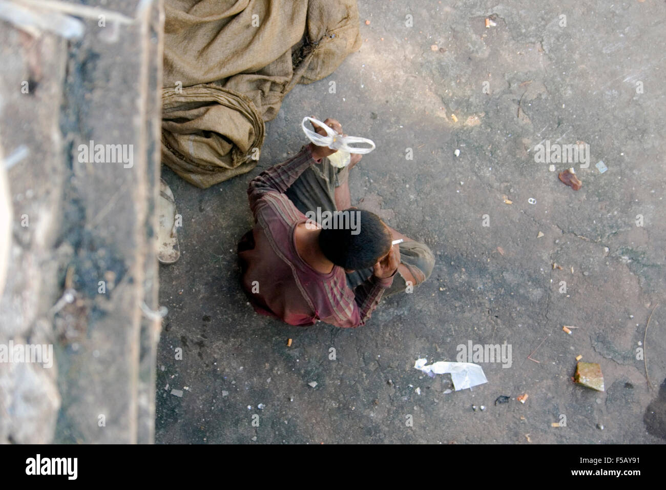 Une chasse l'homme vivant dans la pauvreté est assis sur un trottoir alors qu'il renifle la colle & fume une cigarette à Kampong Cham, au Cambodge. Banque D'Images