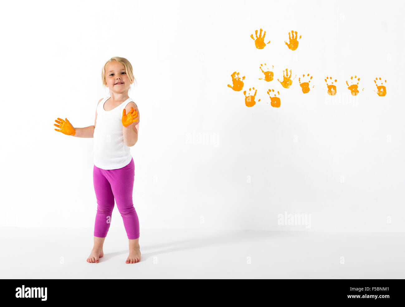 Petite fille peinture mur blanc avec des couleurs orange et handprints Banque D'Images