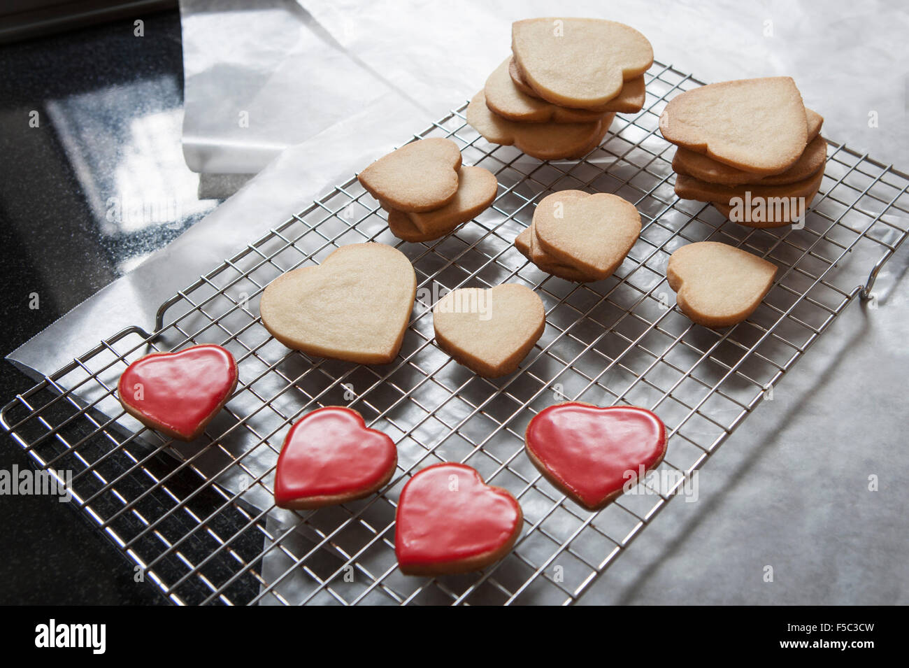 Petits et grands Sablés Heart-Shaped sur grille de refroidissement, certaines avec glaçure rouge Banque D'Images