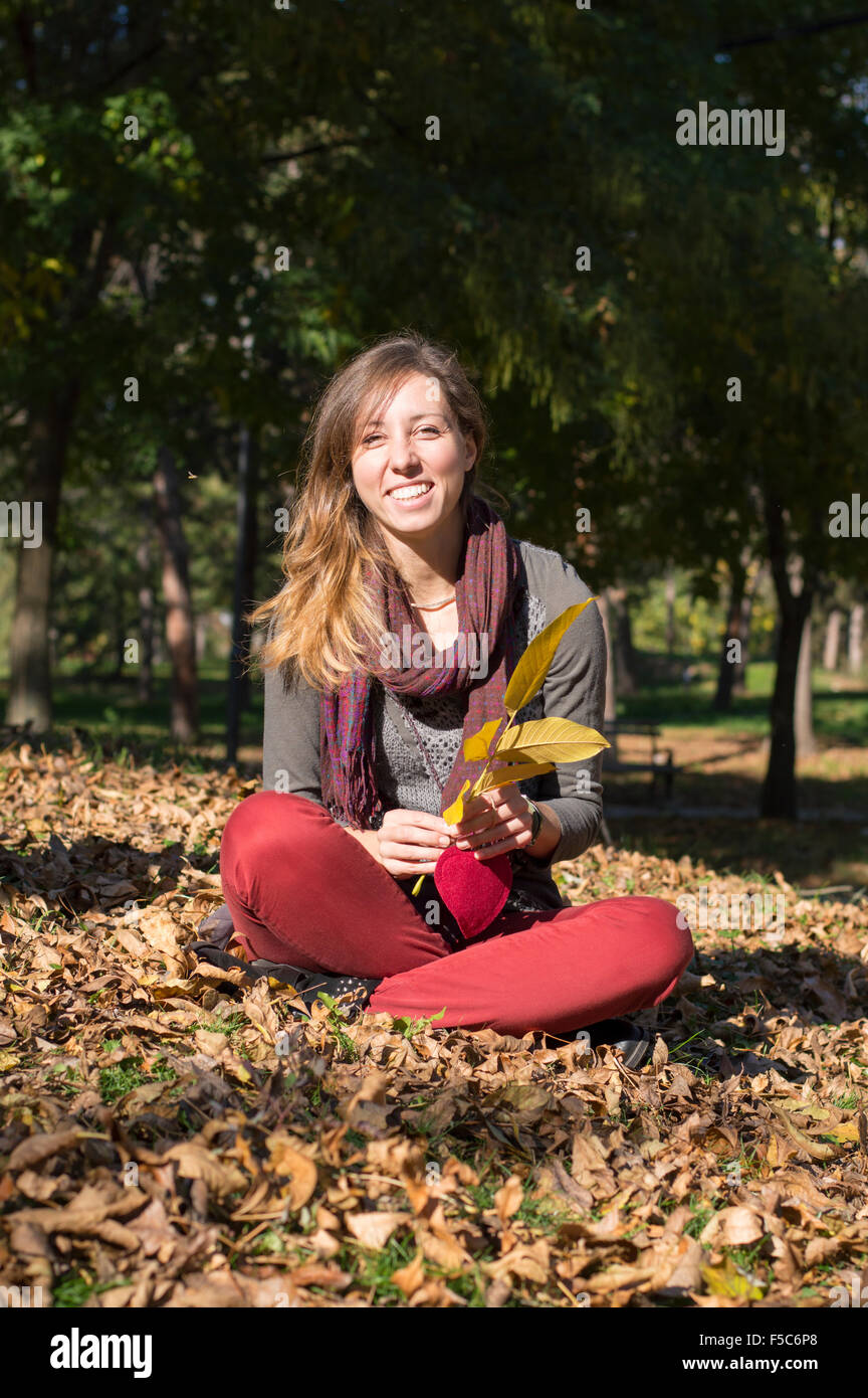 Happy brunette fille assise dans le parc entre les feuilles d'automne jaune Banque D'Images