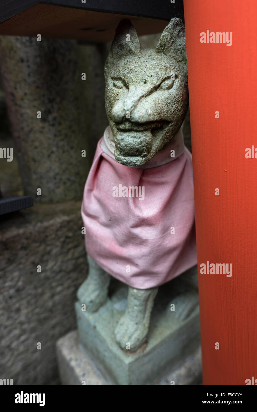 Statue d'un renard avec une balle dans la gueule à côté d'une porte torii au sanctuaire Fushimi Inari Taisha, Kyoto, Japon Banque D'Images
