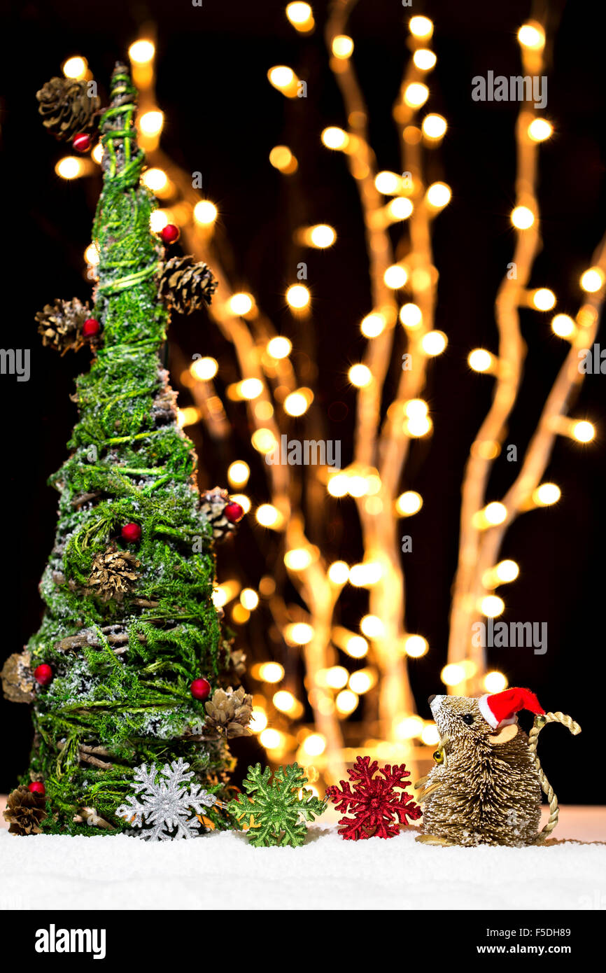 Un bébé souris dans Santa hat avec flocons assis près de l'arbre de Noël sur un arrière-plan flou de nuit. Banque D'Images