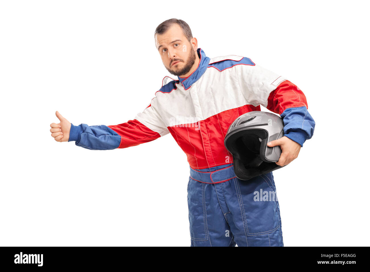 Portrait d'un jeune homme dans un costume racer tenant un casque et l'auto-stop avec son pouce isolé sur fond blanc Banque D'Images