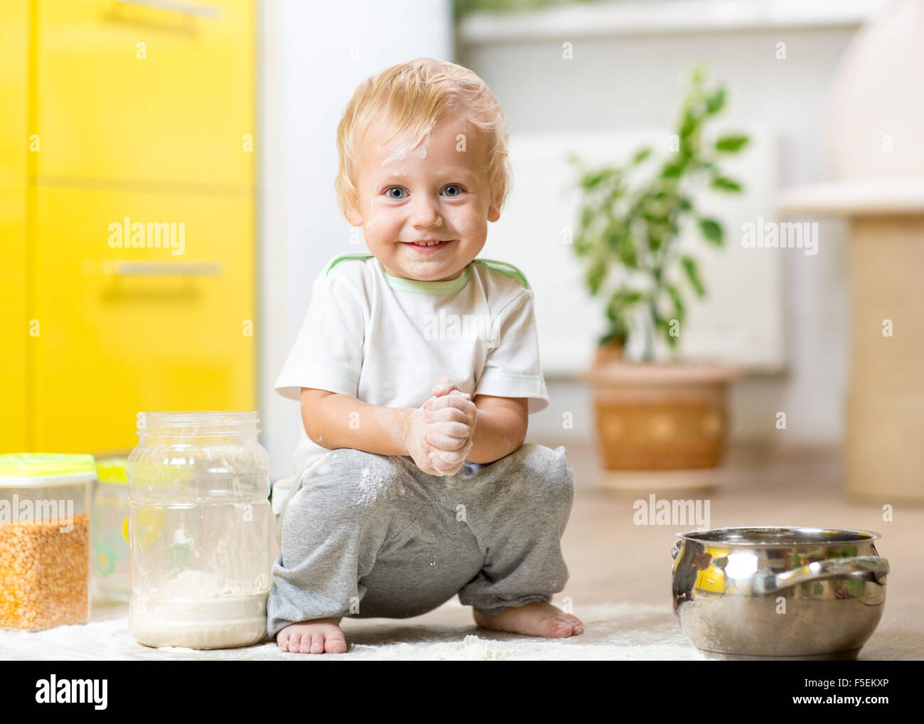 Tout-petit enfant espiègle face avec la farine sale. Petit garçon entouré ustensiles et les denrées alimentaires Banque D'Images