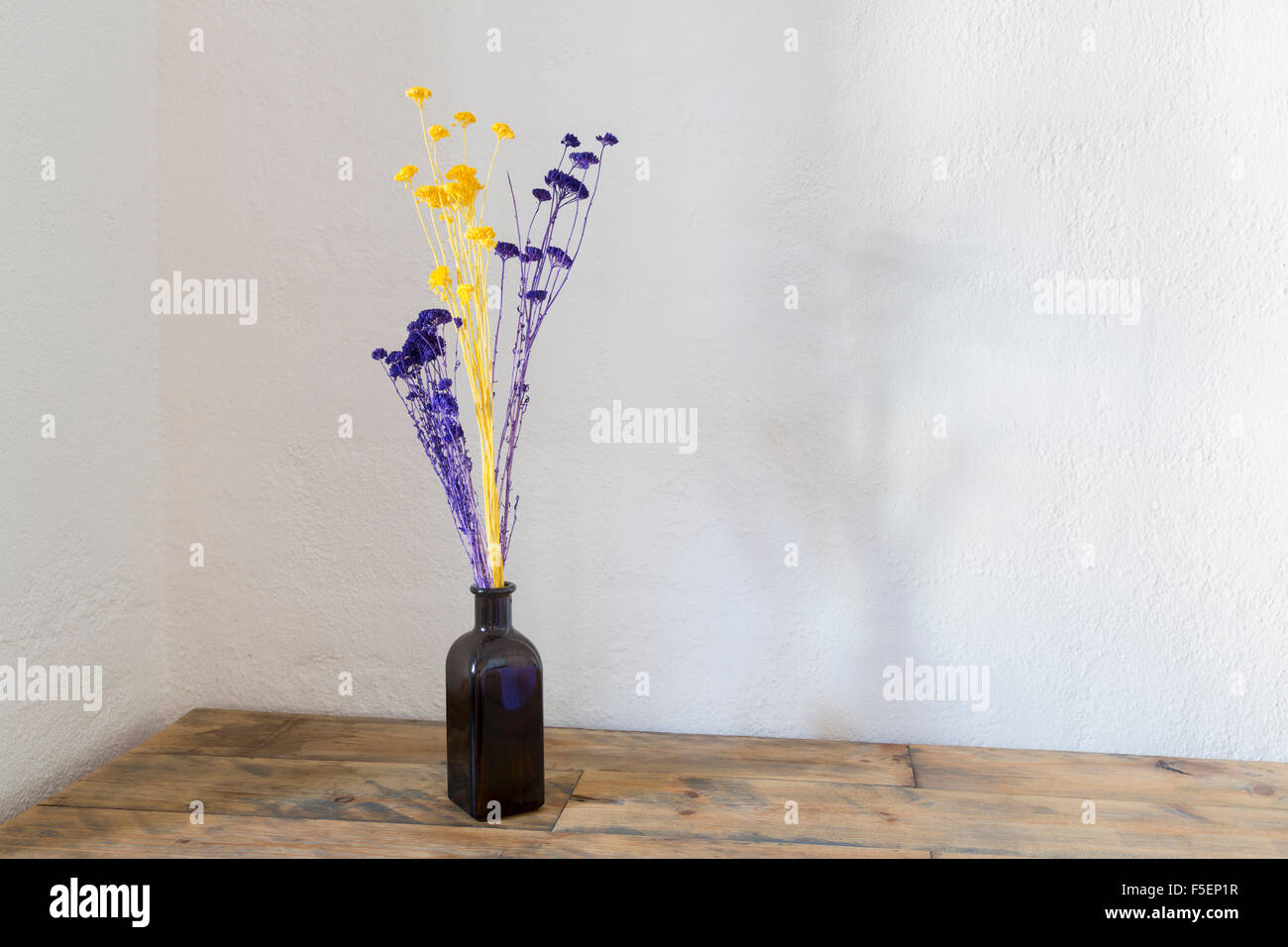 Violet et jaune fleurs séchées dans un vase bouteille bleu sur une vieille table en bois Banque D'Images