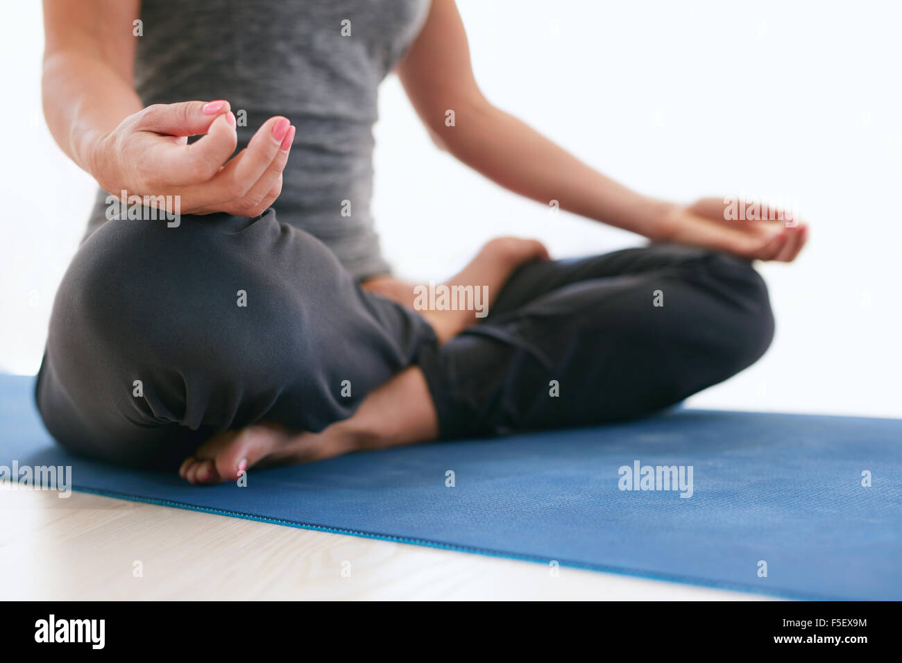 Close up of female sitting cross legged et mains sur les genoux lors de la méditation. Woman sitting in Lotus pose sur tapis d'exercice à la salle de sport Banque D'Images