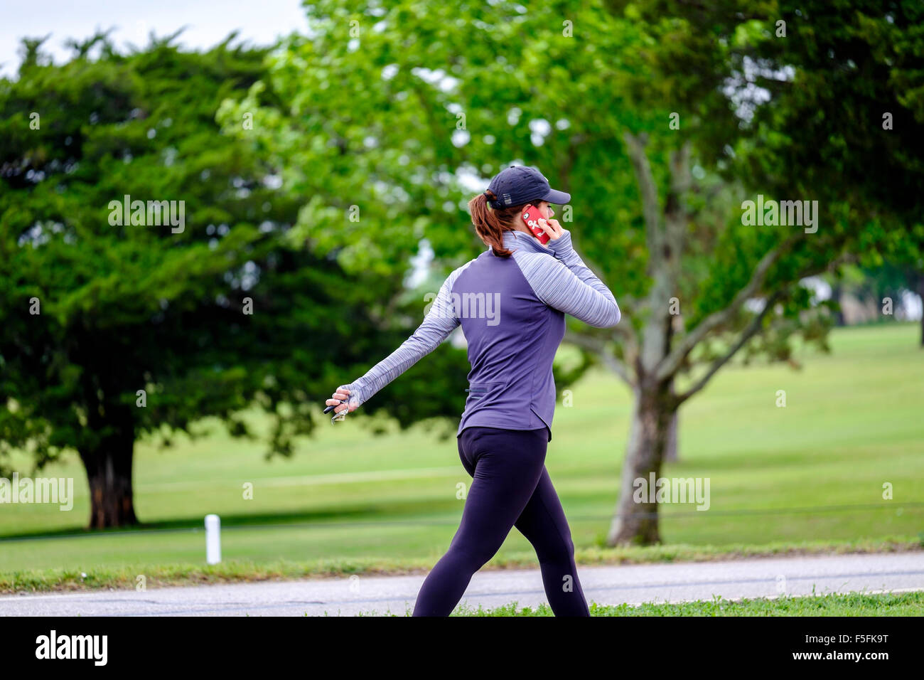 Une femme de race blanche dans la trentaine parle sur son téléphone cellulaire pendant l'exercice à un parc public à Oklahoma City, Oklahoma, USA. Banque D'Images