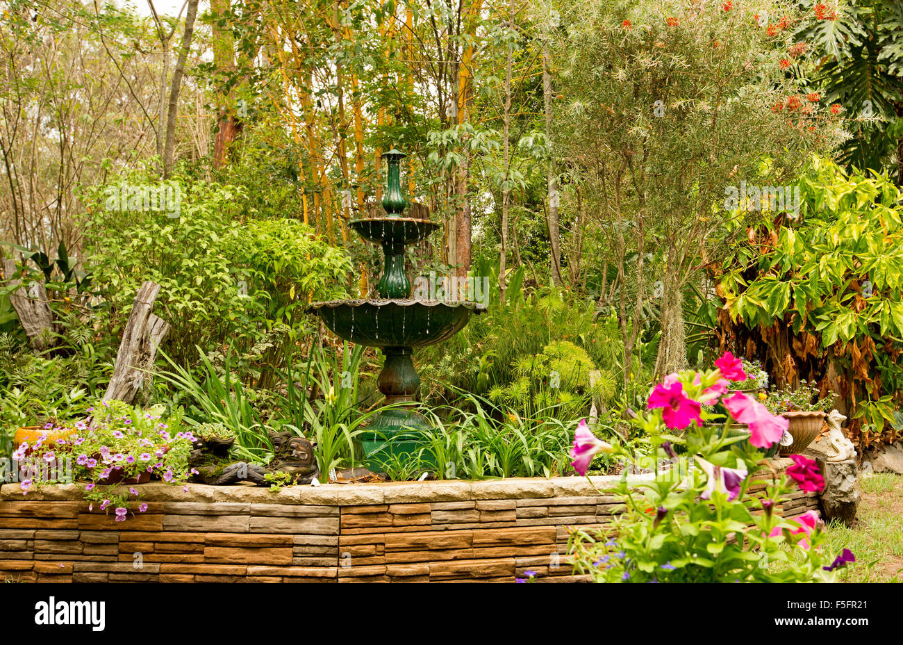 Jardin décoratif avec muret en pierre, ornate fountain et végétaux dans des conteneurs, ourlée par des arbustes, bambous et grands arbres Banque D'Images