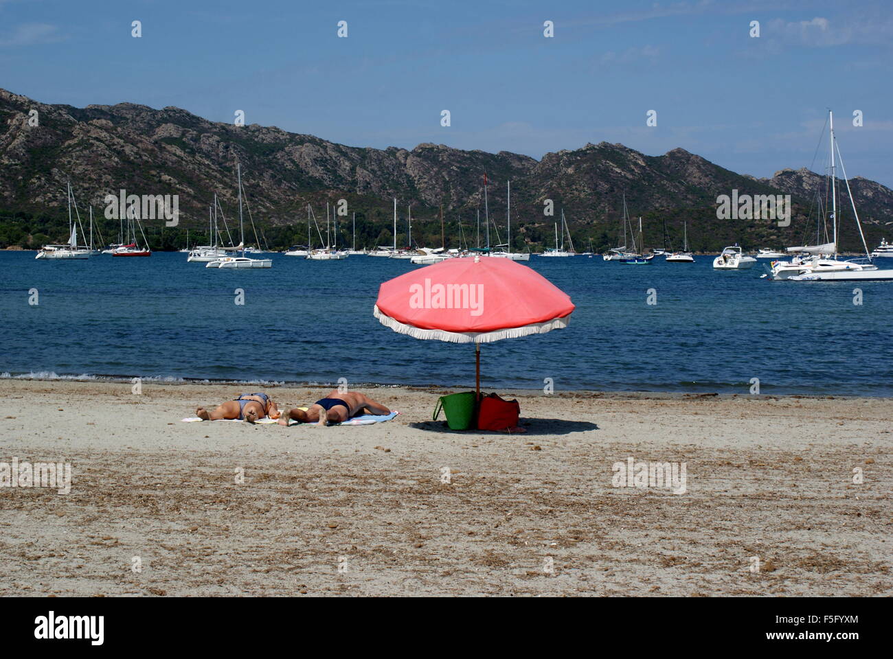 Deux personnes de soleil sur Saint Florent plage près d'un parapluie rose Banque D'Images