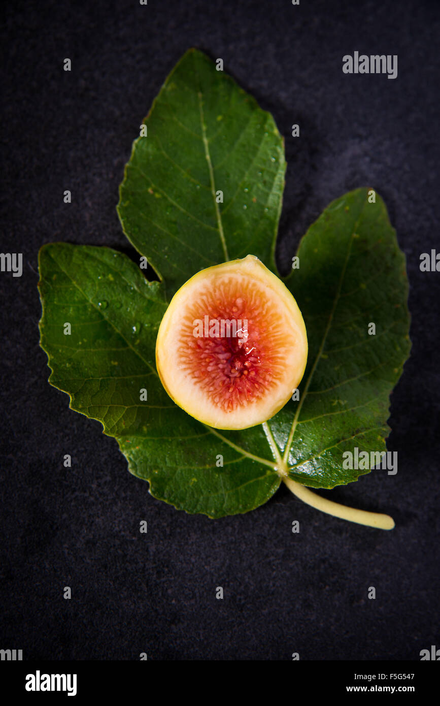 Un nouveau schéma réduit de moitié avec une feuille de vigne sur un fond sombre. Ces petites figues italiennes sont très doux et délicieux ! Banque D'Images
