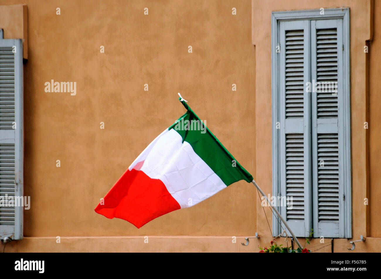 Drapeau Italien qui flottent dans le vent sur le côté de la construction traditionnelle avec volets en bois gris à Rome, Italie Banque D'Images