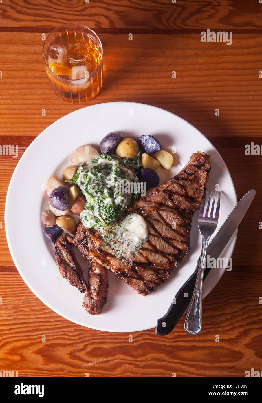 Vue aérienne de steak avec pommes de terre et épinards couteau et fourchette et cocktail sur la table en bois Banque D'Images