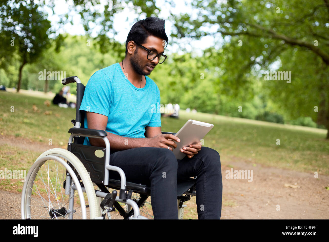 Jeune Indien homme en fauteuil roulant à l'aide d'un ordinateur tablette Banque D'Images