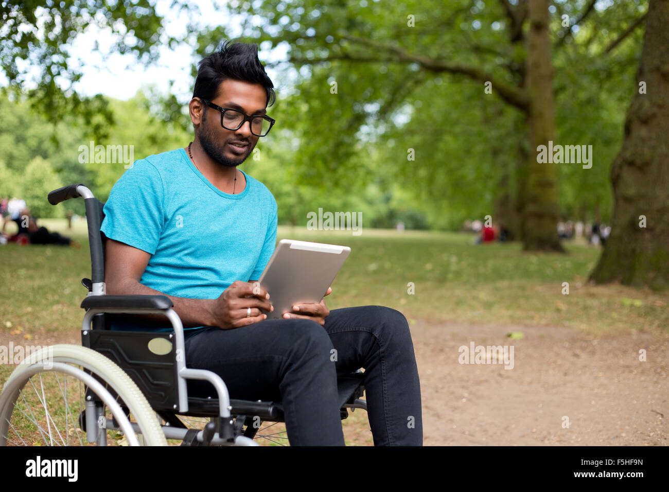 Jeune Indien homme en fauteuil roulant à l'aide d'un ordinateur tablette Banque D'Images