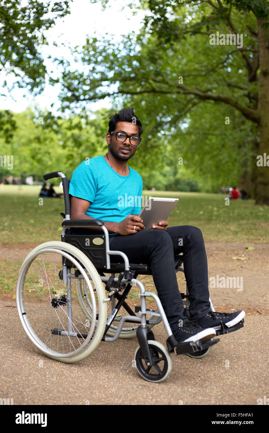 Jeune homme en fauteuil roulant à l'aide d'un ordinateur tablette Banque D'Images