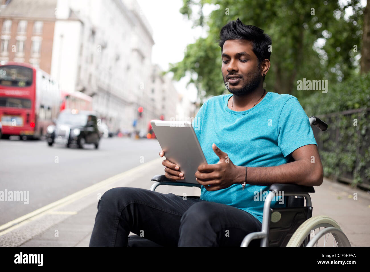 Homme handicapé dans un fauteuil roulant à l'aide d'un ordinateur tablette dans la rue Banque D'Images