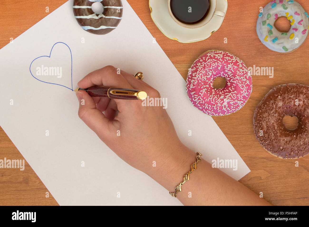 La femme l'écriture d'un symbole de cœur sur un document du bureau avec des beignets et du café sur une table. Banque D'Images