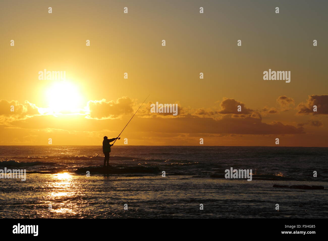 Un homme d'une quarantaine de pêche les rochers à Scarbrough en NSW, Australie au lever du soleil. Banque D'Images