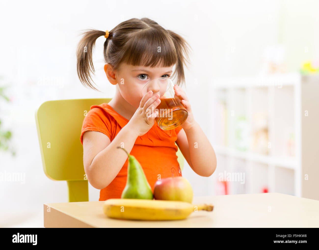 Smiling enfant fille assise sur la table avec des fruits et boire du jus in nursery Banque D'Images