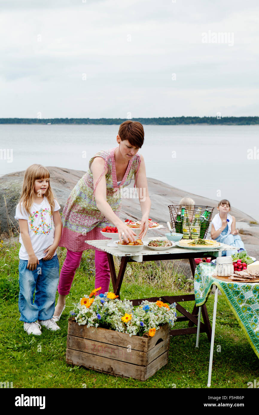 La Suède, l'Uppland, Roslagen, femme la préparation d'une table de pique-nique au bord de mer Banque D'Images
