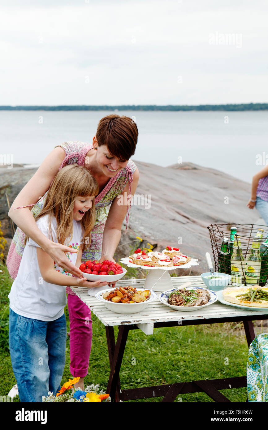 La Suède, l'Uppland, Roslagen, femme la préparation d'une table de pique-nique au bord de mer Banque D'Images