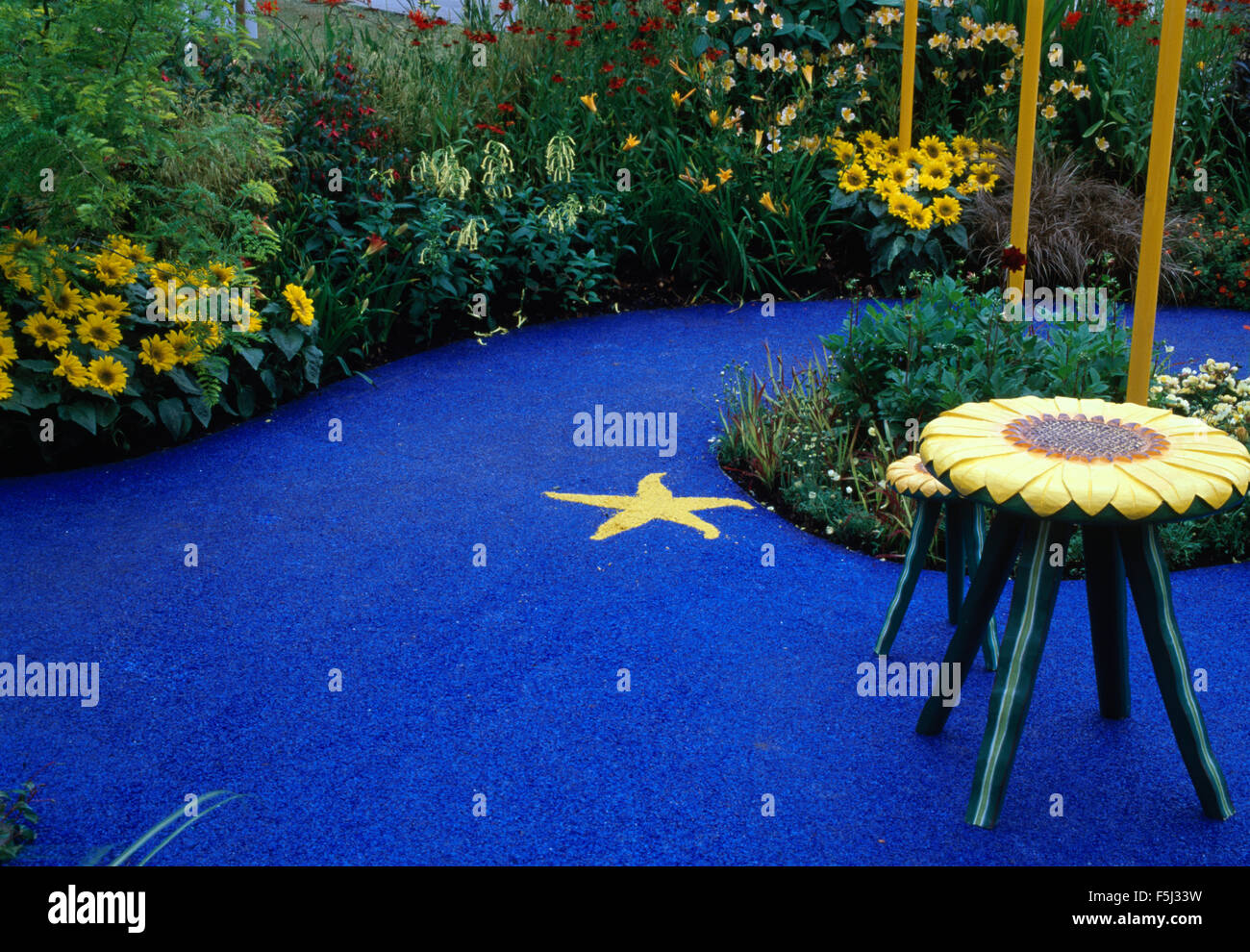 Tabourets en forme de tournesol sur un patio circulaire bleu vif avec tournesols jaunes en bordure Banque D'Images