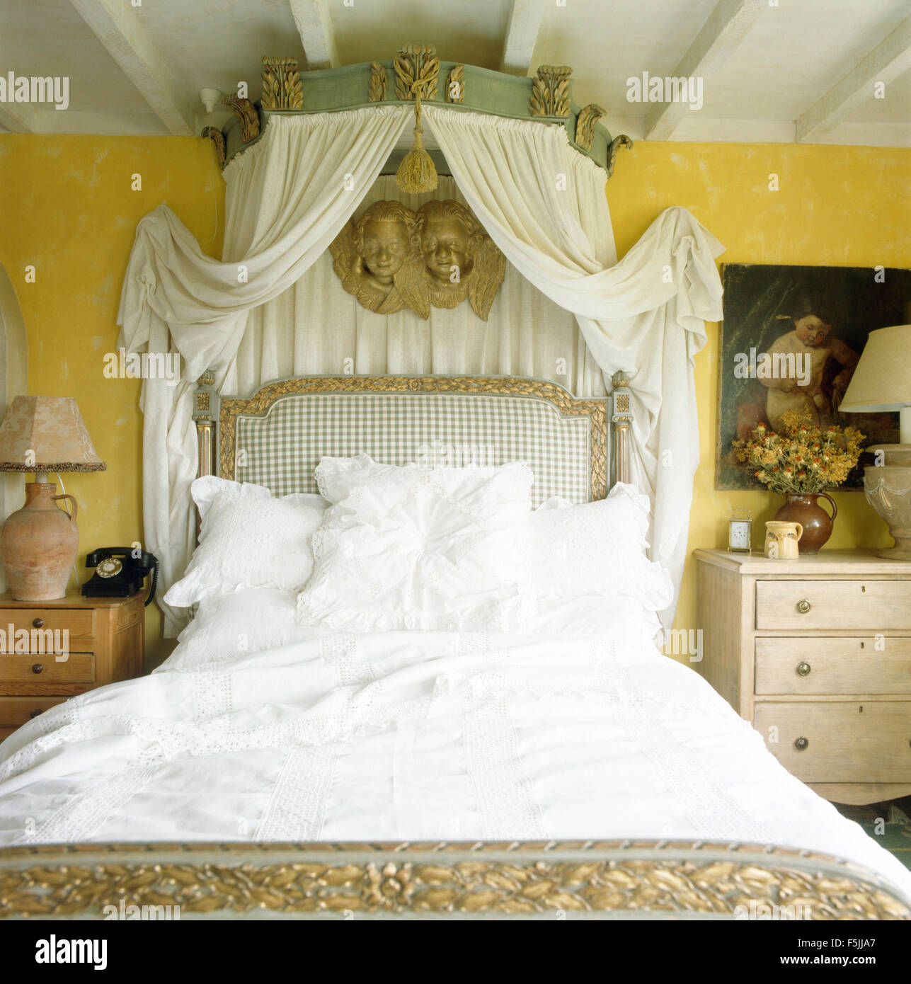 Auvent orné avec des rideaux blancs sur lit avec draps garnis de dentelle dans une chambre jaune années 80 Banque D'Images