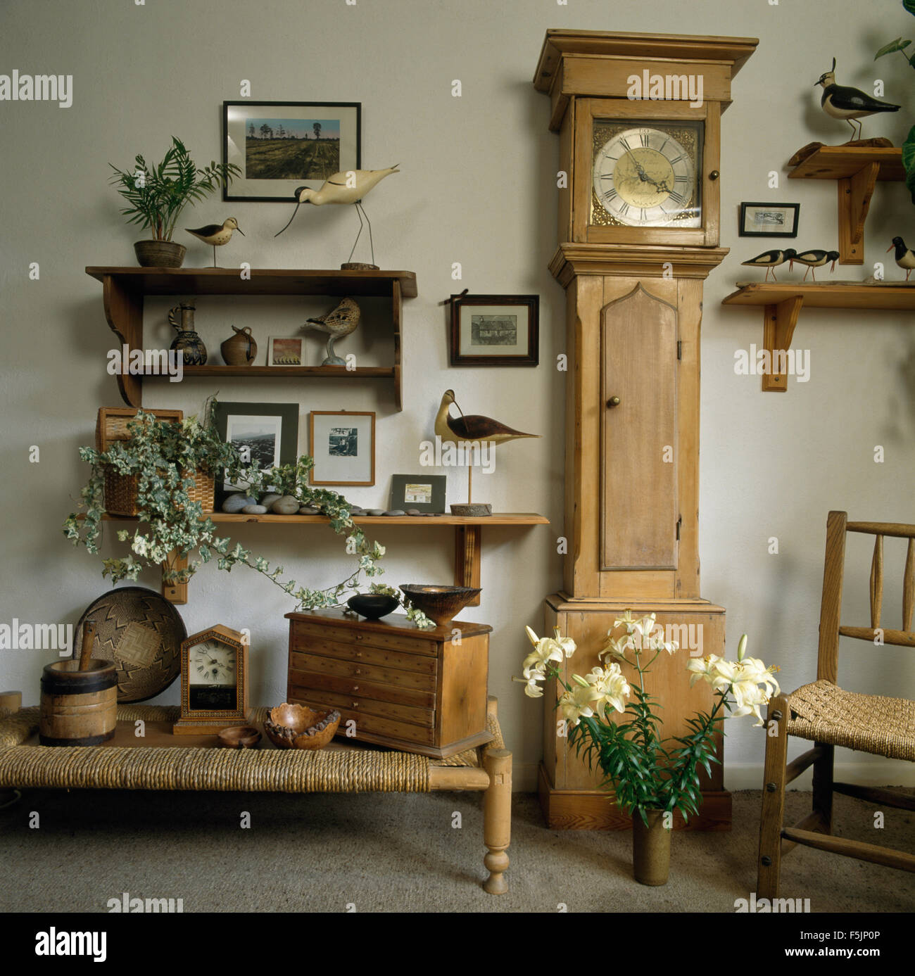 Horloge de parquet en pin et un faible tabouret en rotin années 90 dans une salle à manger avec collection d'oiseaux en bois sur les petites tablettes Banque D'Images