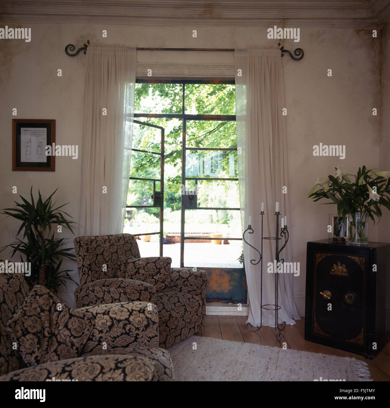 Vieux coffre-fort utilisé comme une table dans un salon avec des rideaux de voile blanc sur Crittall windows en français Banque D'Images
