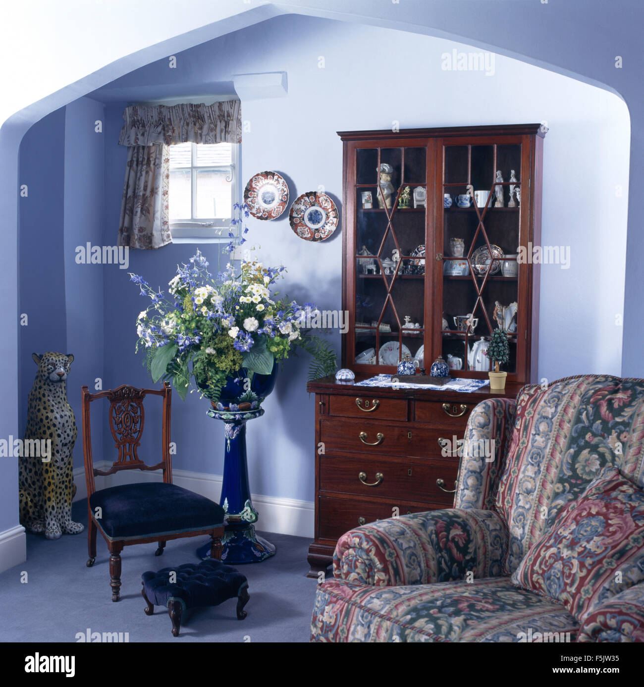 Fauteuil à motifs et mobilier en bois commode dans un bleu 90 salon avec un arrangement floral d'été sur un piédestal de la Chine Banque D'Images