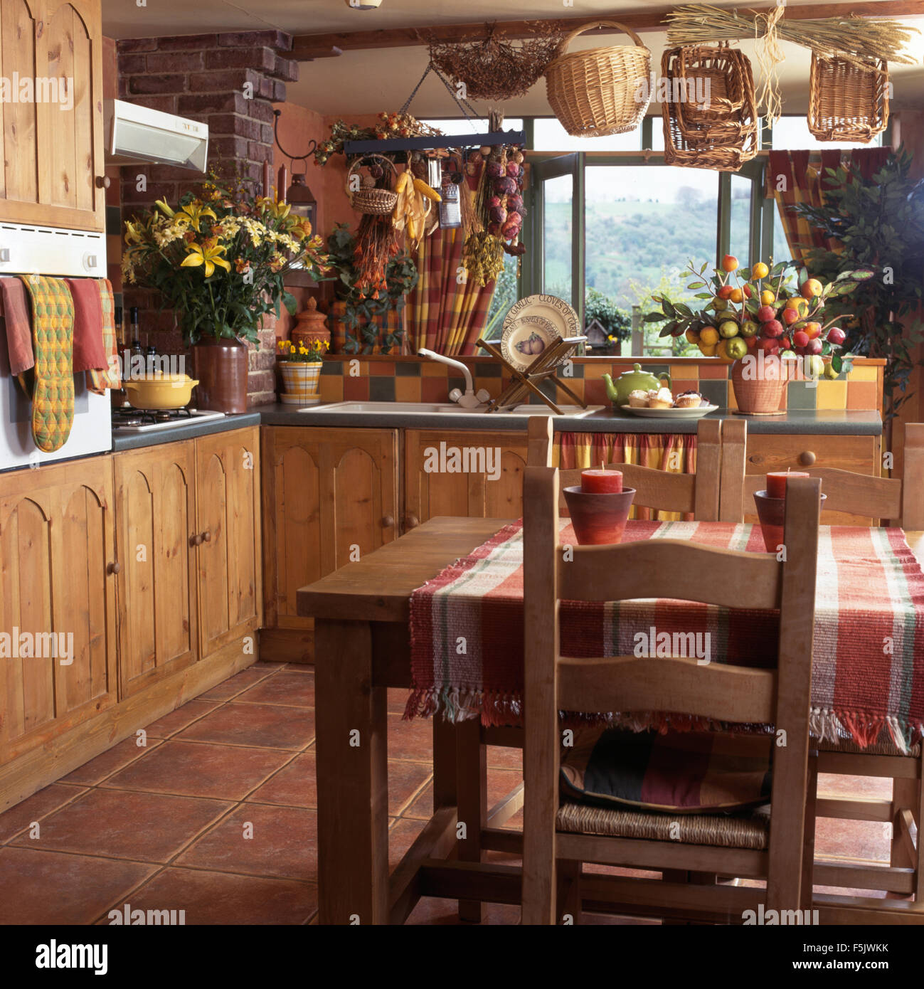 Chaises en bois rustique à table avec un chiffon contrôlée dans un pays cuisine avec portes en pin sur des unités montées et paniers au plafond Banque D'Images