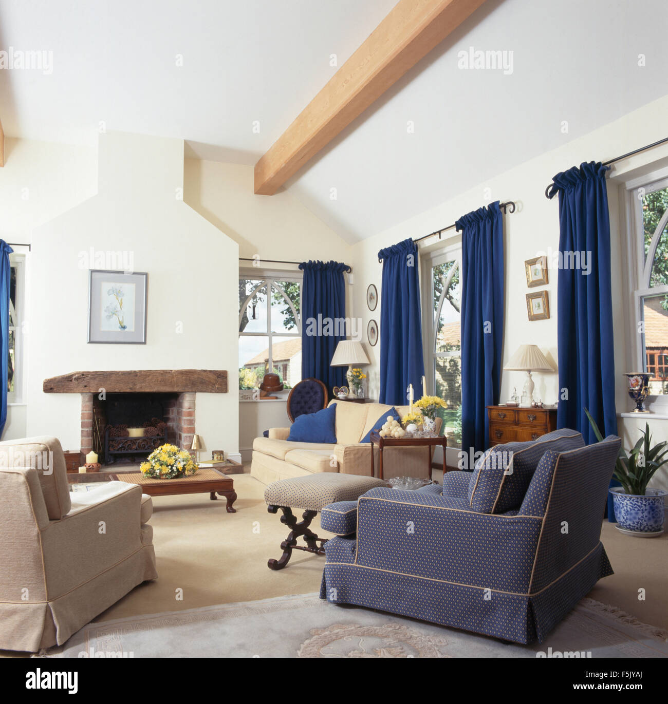 Fauteuils bleus et crème et crème canapé situé autour de la cheminée dans un salon l'extension avec des rideaux bleus sur la fenêtre Banque D'Images