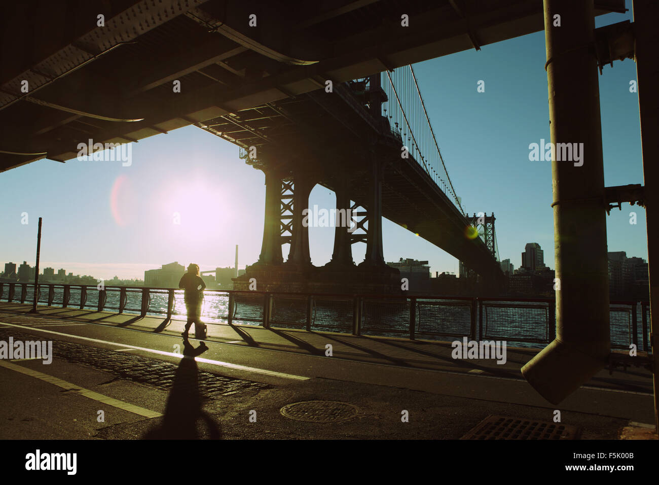 Un runner décale l'East River Esplanade sous pont de Manhattan comme le soleil se lève Banque D'Images