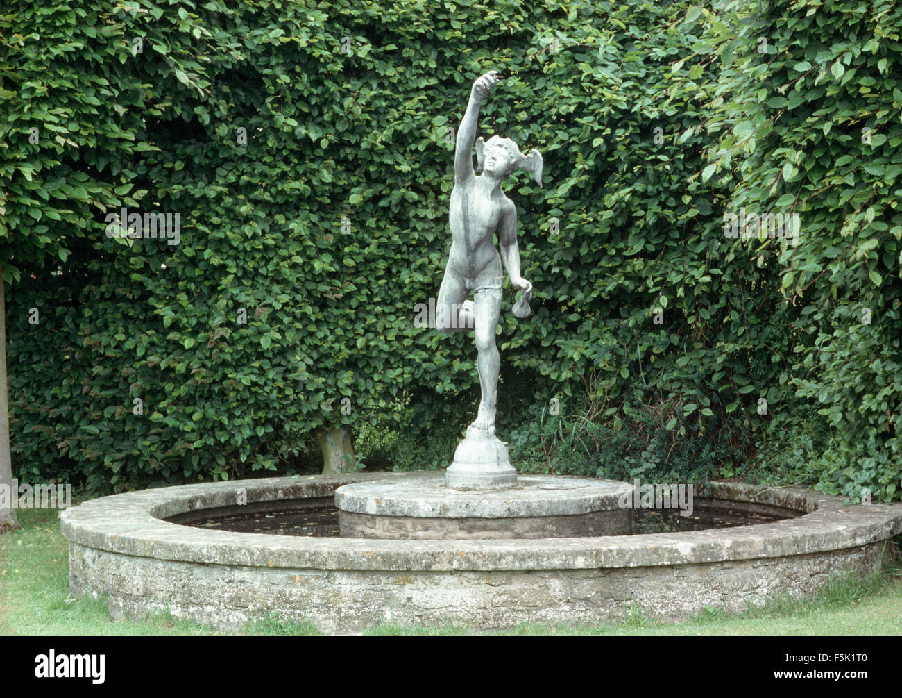 Statue classique dans le centre d'un bassin circulaire en pierre contre une haie coupée Banque D'Images