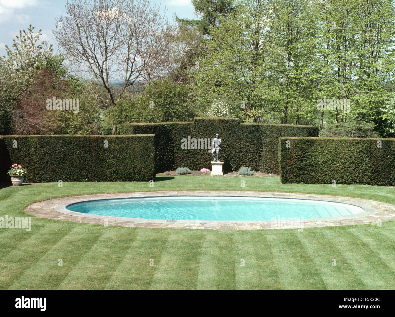 Piscine turquoise circulaire situé dans une pelouse récemment fauché avec une grande couverture tronquée entourant une statue classique Banque D'Images