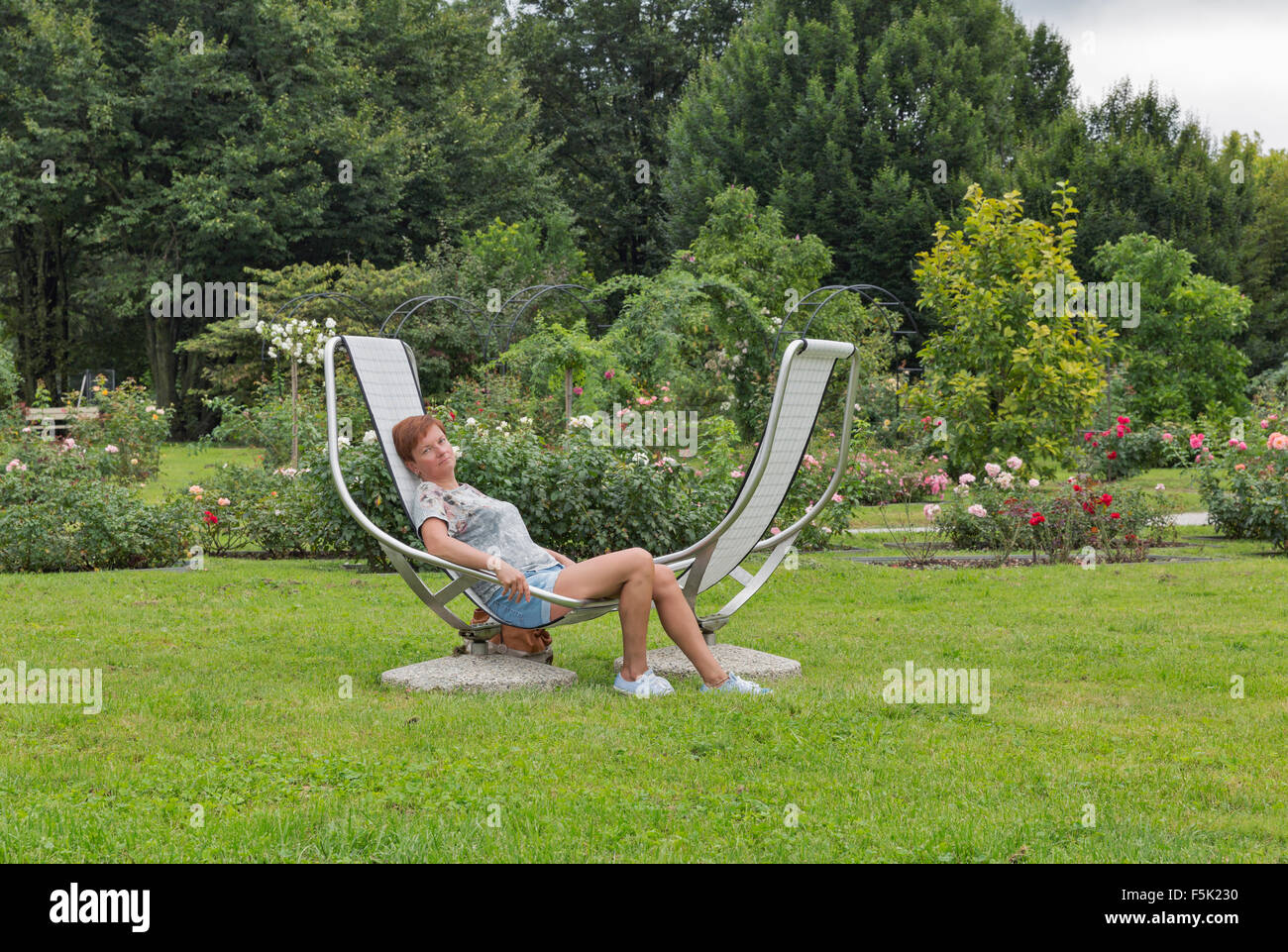 Middle aged woman sitting on président fixes pour les loisirs de plein air en face du jardin de roses Banque D'Images