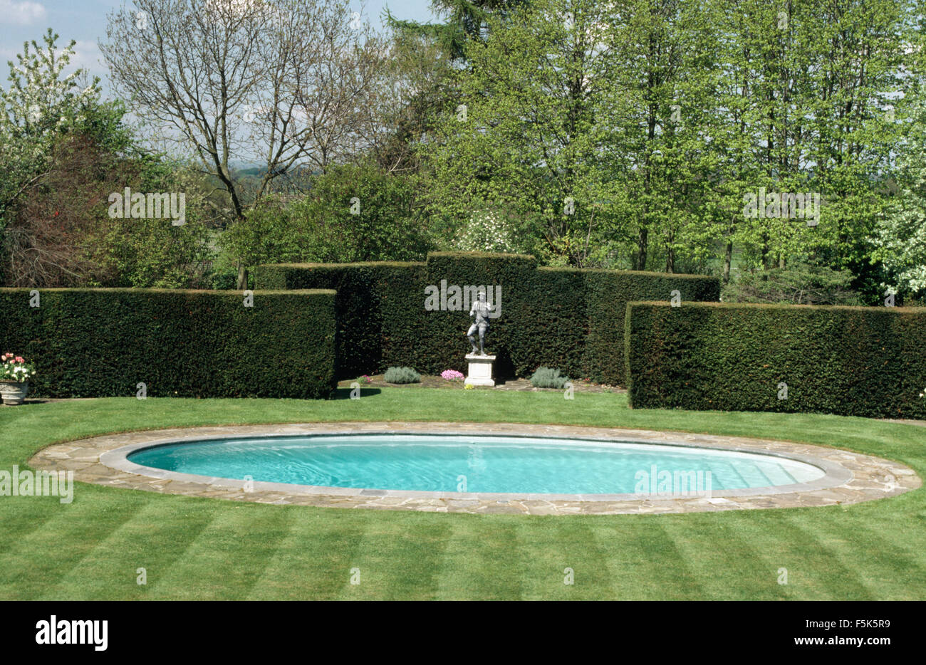 Piscine circulaire et la statue de pierre sur une plinthe en face d'une haute haie taillés dans de grands pays jardin Banque D'Images