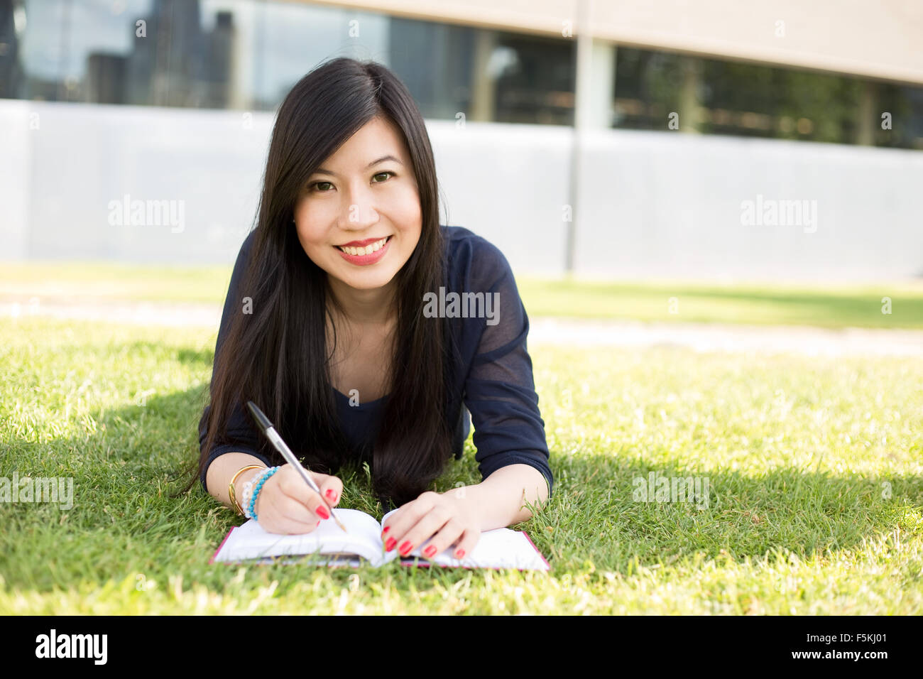 Jeune étudiant japonais couché dans l'herbe avec un livre Banque D'Images