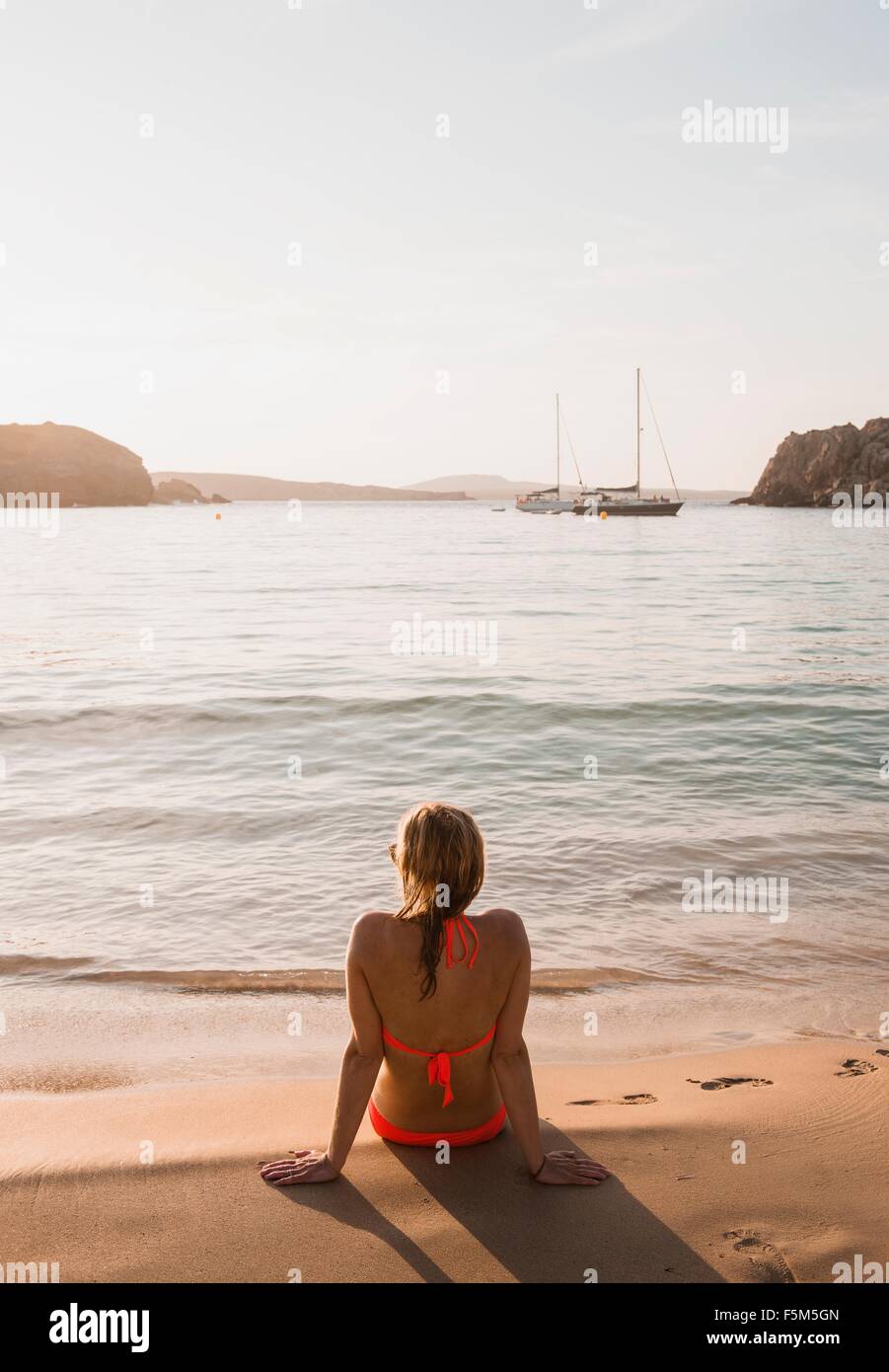 Vue arrière de femme assise à la recherche de plage, Minorque, Iles Baléares, Espagne Banque D'Images