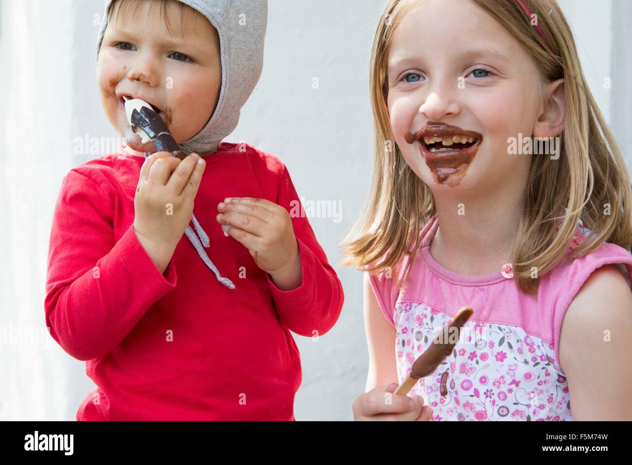 Female toddler et salissent soeur manger du chocolat glaces Banque D'Images