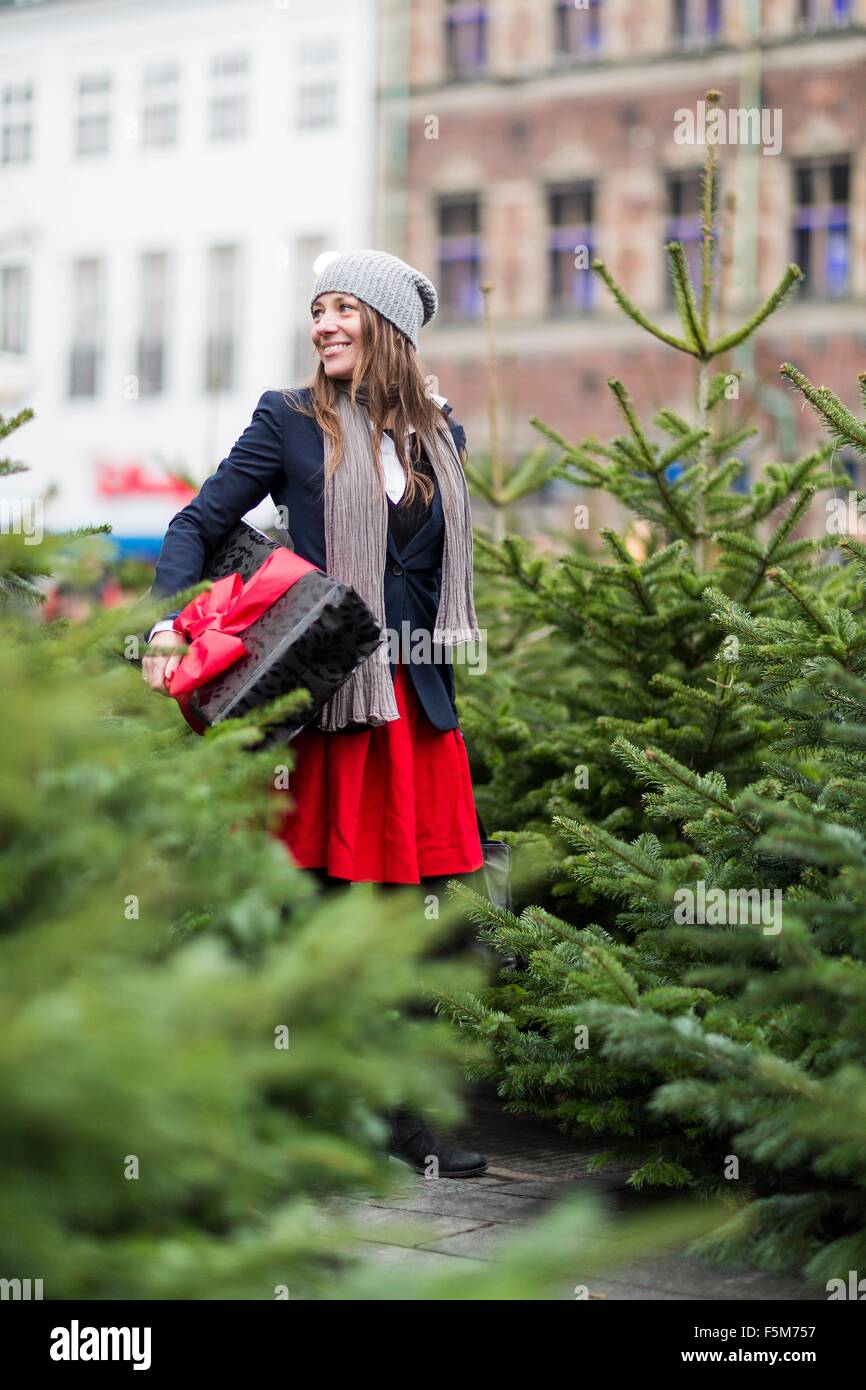 Femme mature avec cadeau de Noël parmi des arbres de Noël Banque D'Images