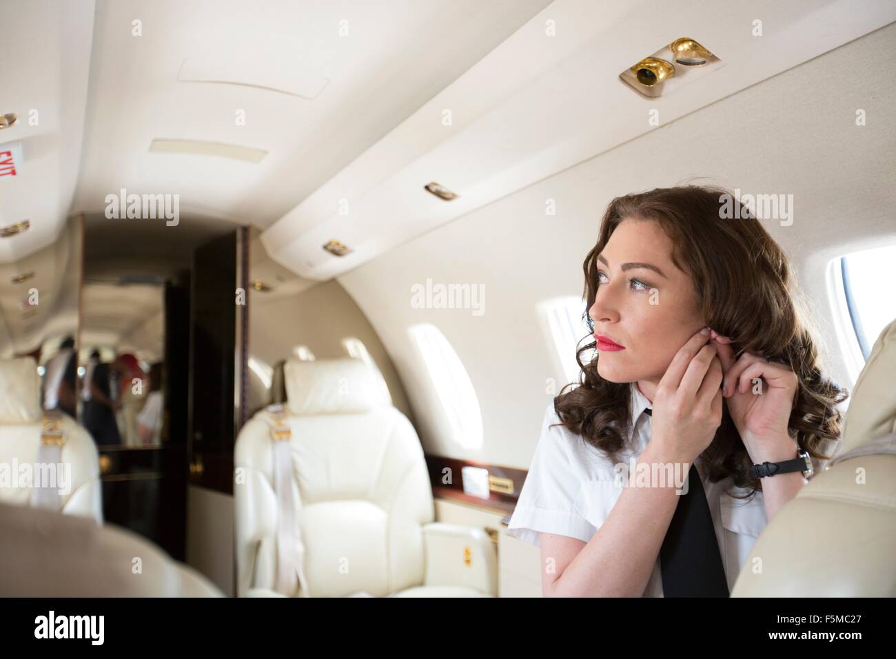 Agent de bord féminin mise sur earring en cabine de jet privé Banque D'Images