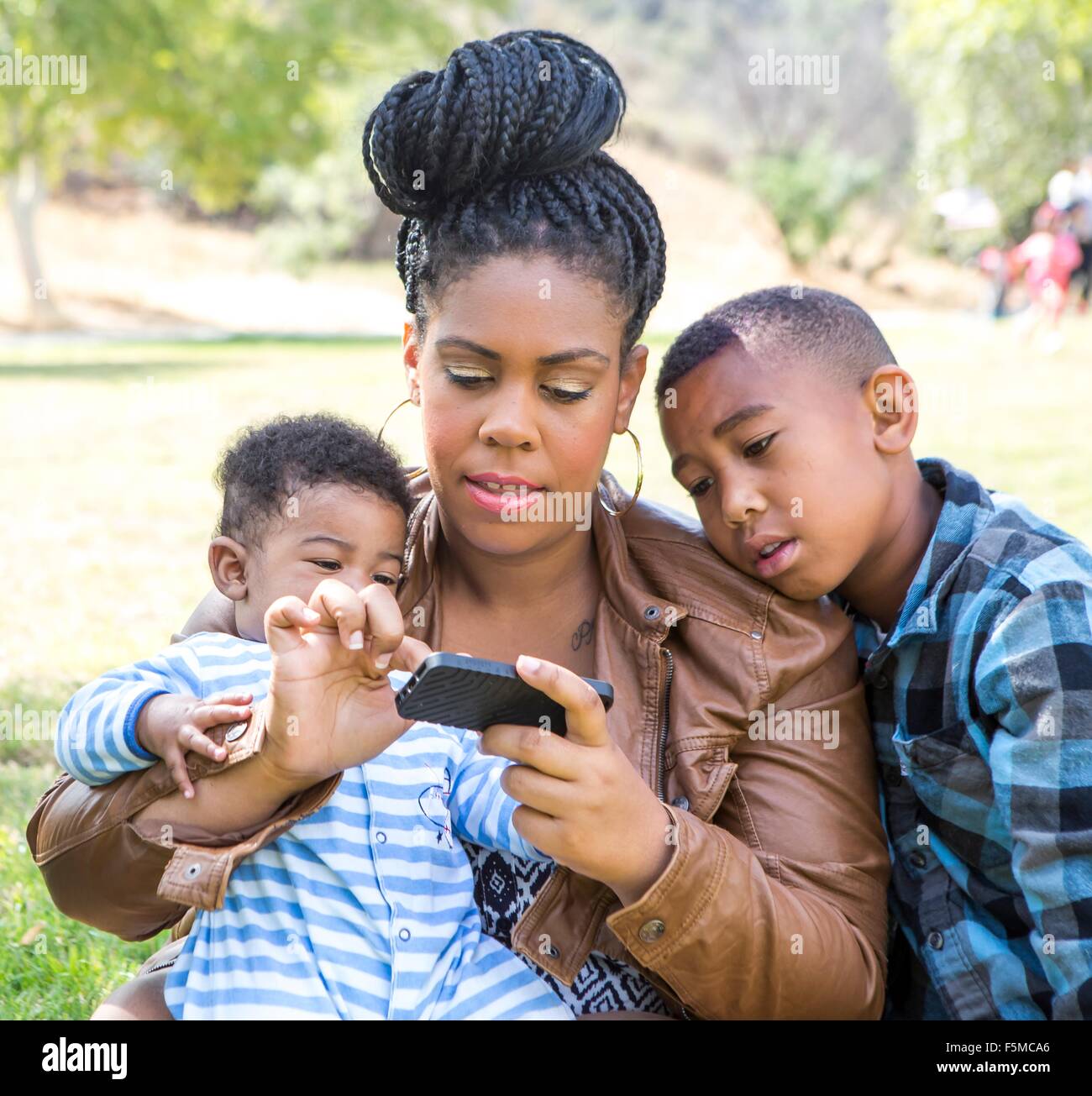 Mère et enfants assis texting on smartphone à bas Banque D'Images