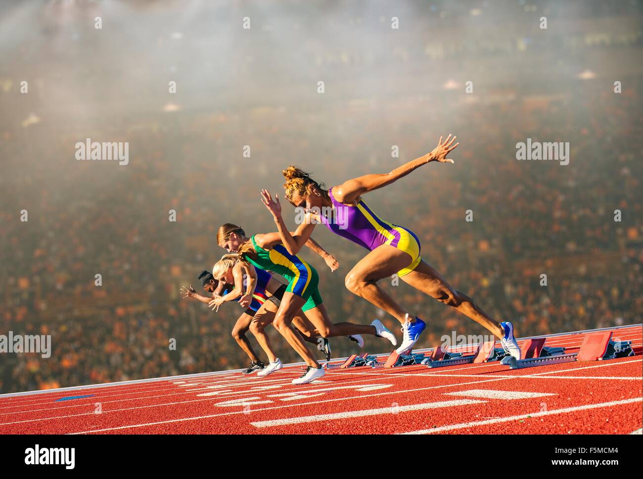Quatre femmes athlètes sur piste d'athlétisme, laissant starting-blocks Banque D'Images