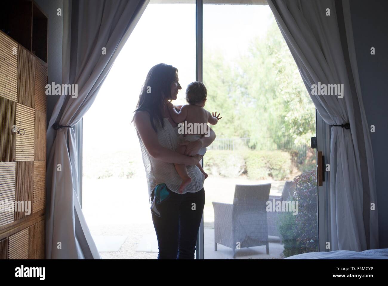 Mother holding baby boy en face de porte patio, looking away Banque D'Images