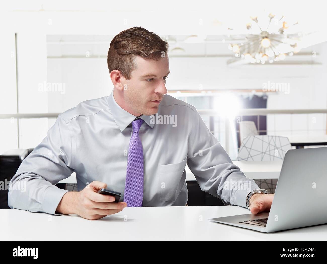 Mid adult businessman sitting at desk, using laptop Banque D'Images