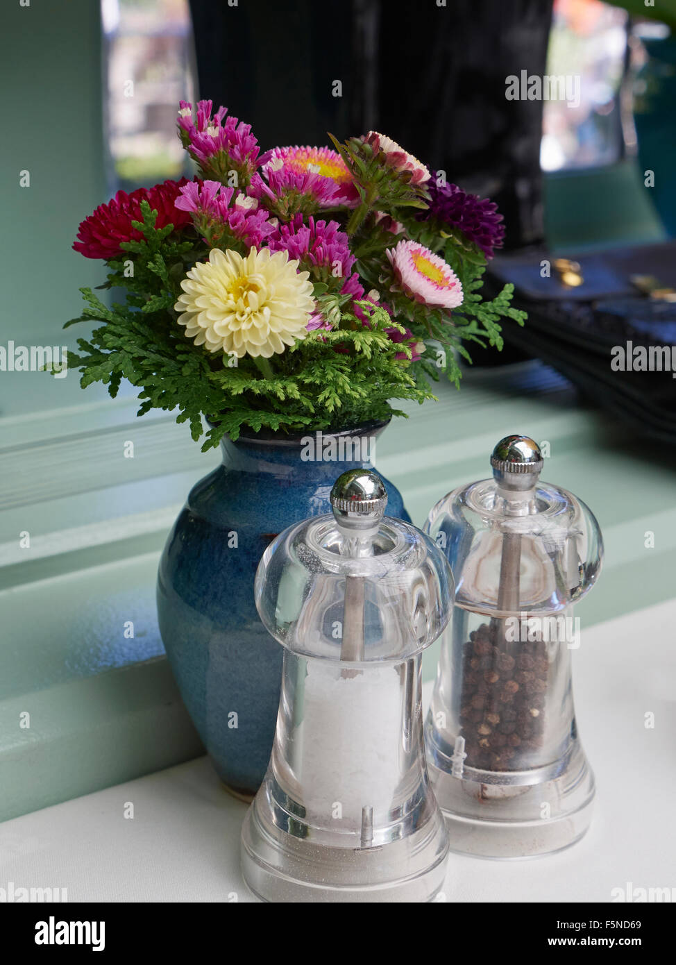 Petit vase de fleurs fraîches avec du sel et moulins à poivre sur une table à manger Banque D'Images