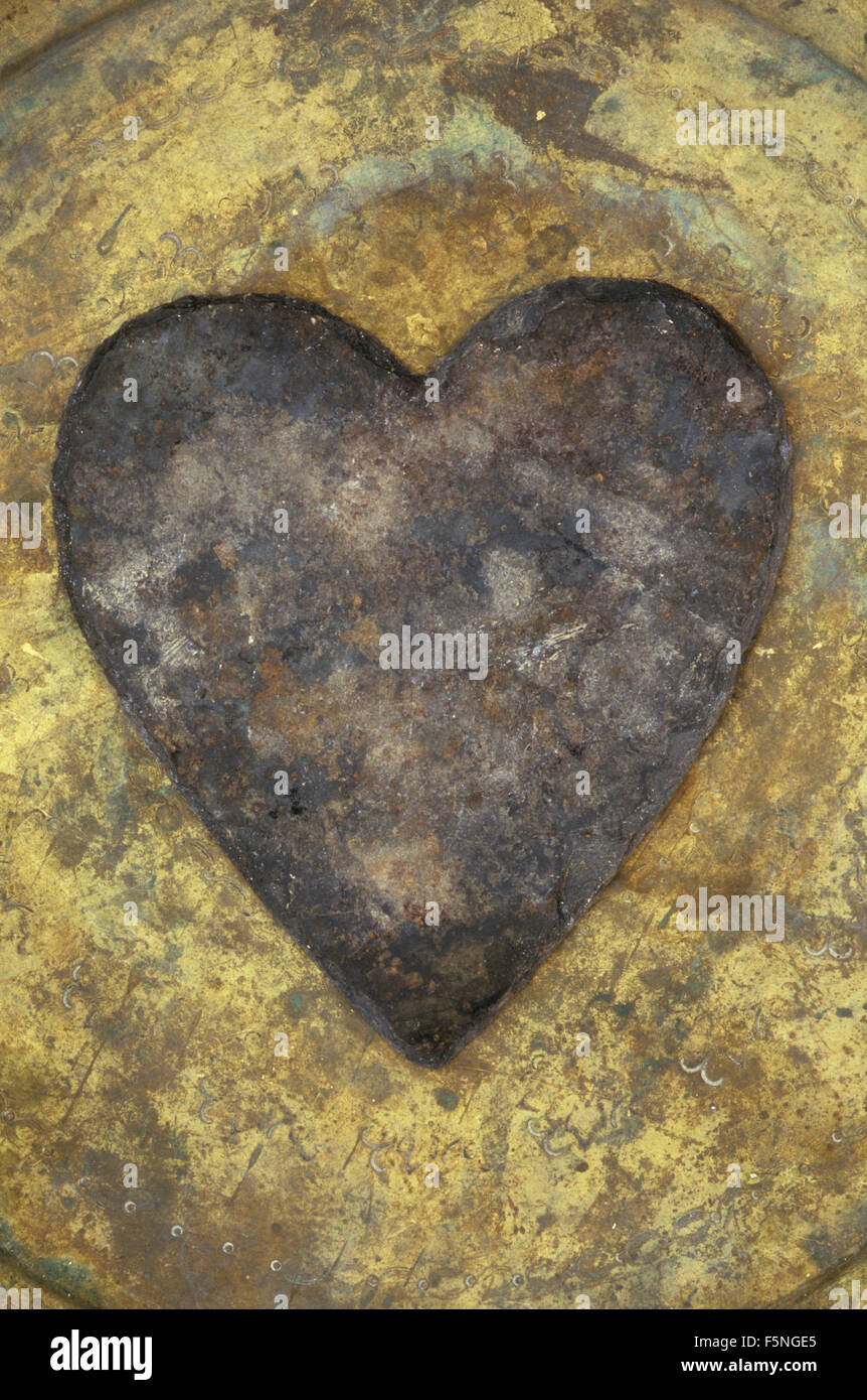 Ardoise gris en forme de cœur avec des marques de rouille brune couchée sur le plateau en laiton à motifs terni Banque D'Images Ardoise gris en forme de cœur avec des marques de rouille brune couchée sur le plateau en laiton à motifs terni Banque D'Images